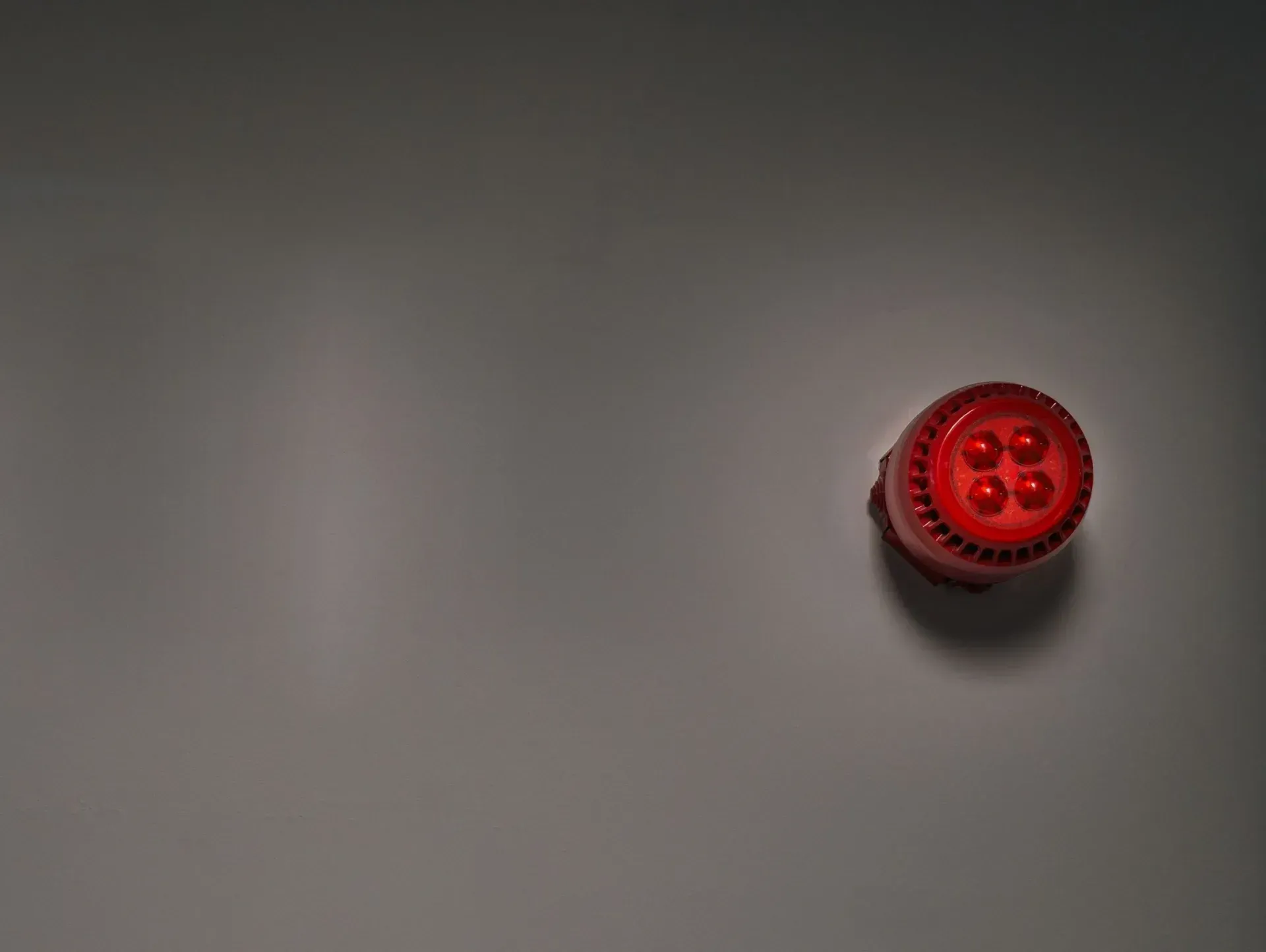 A red fire alarm sounder beacon mounted on a dark grey interior wall