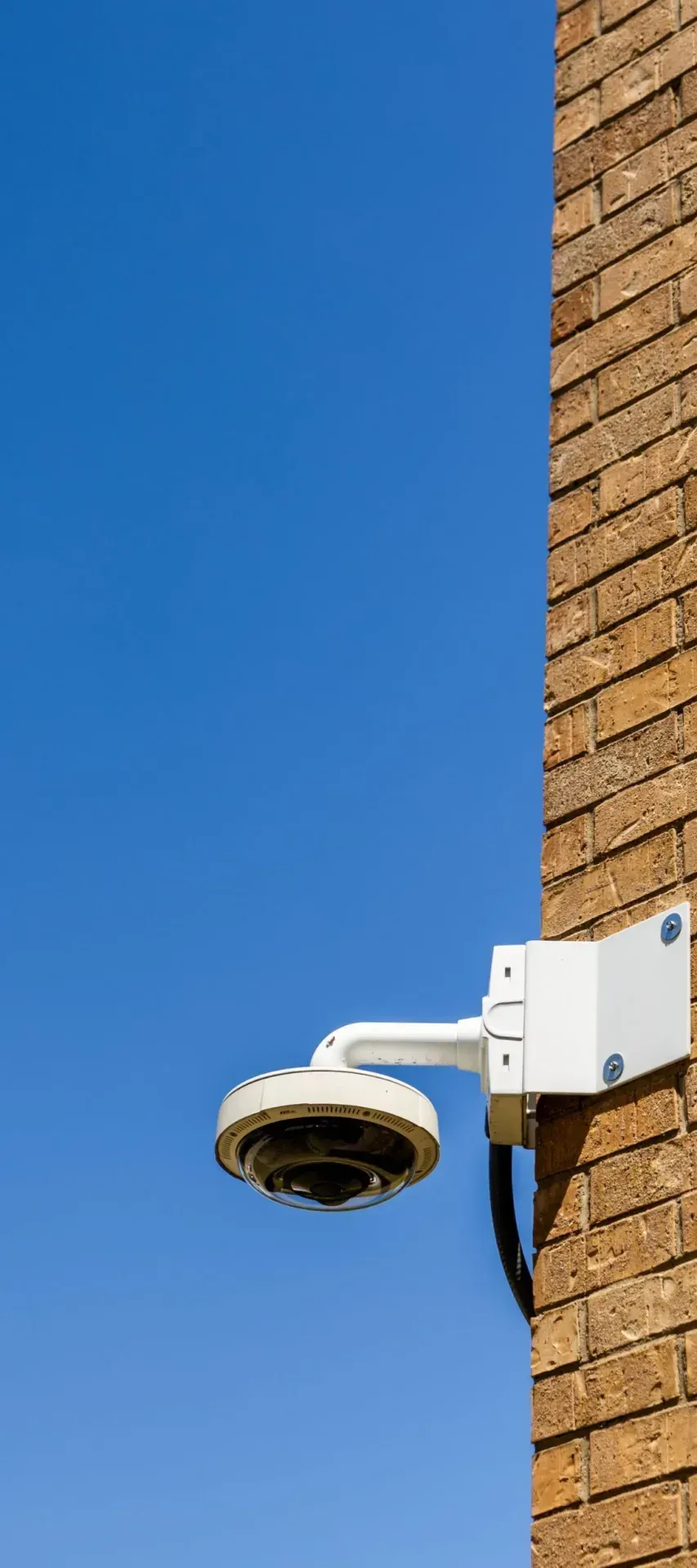 Security camera on a brick wall against a blue sky