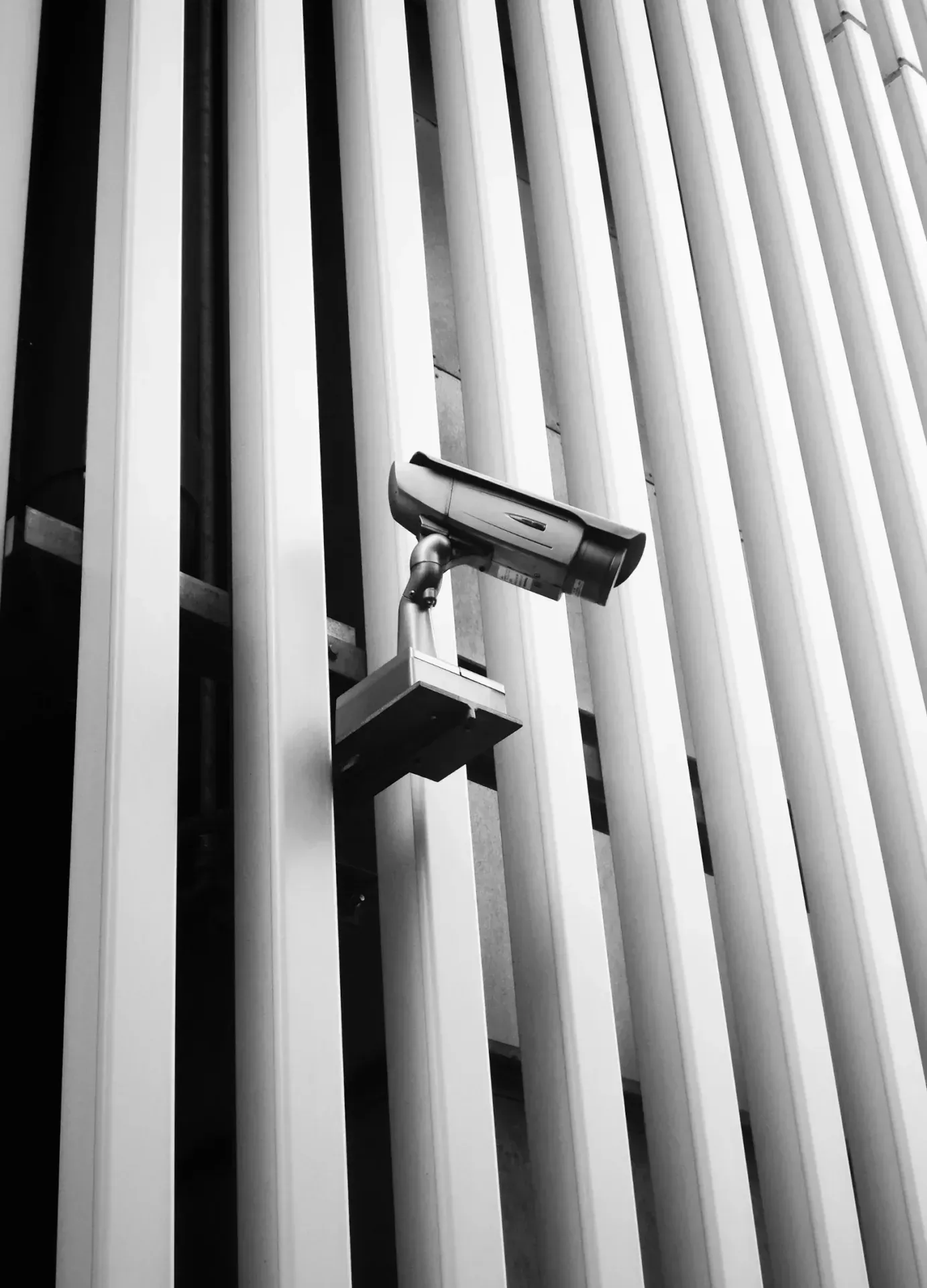 Security camera on a bracket between the vertical fins of a building.