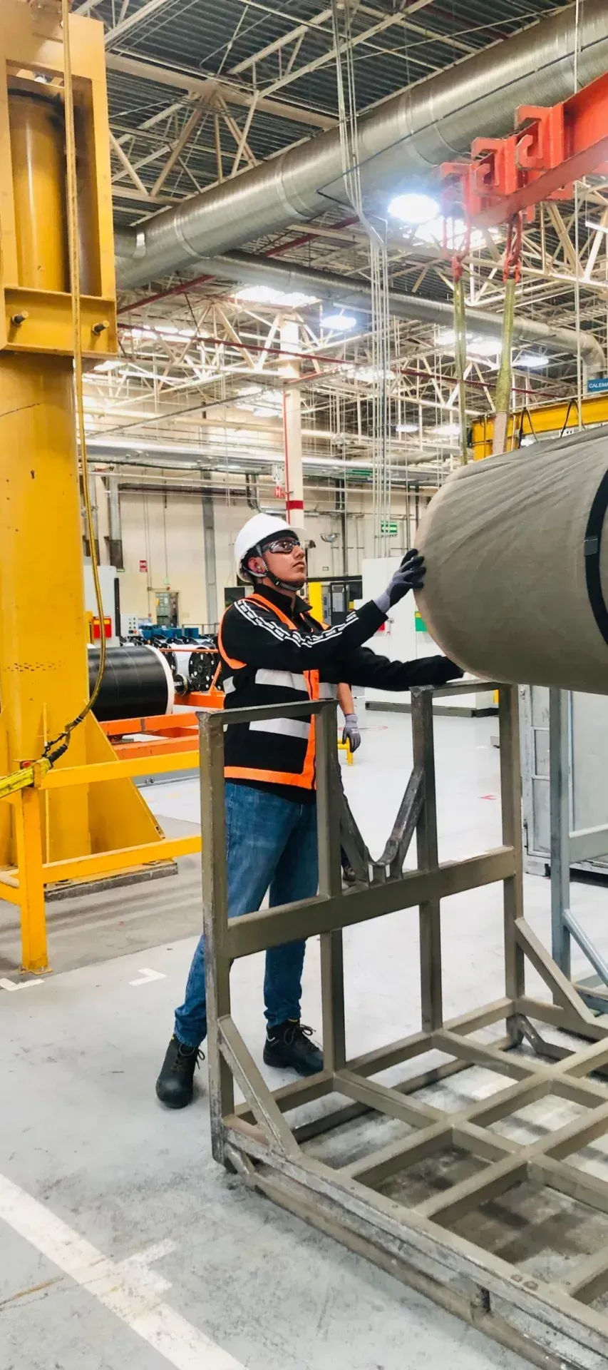 Factory worker in a helmet and high-visibility vest at a machine