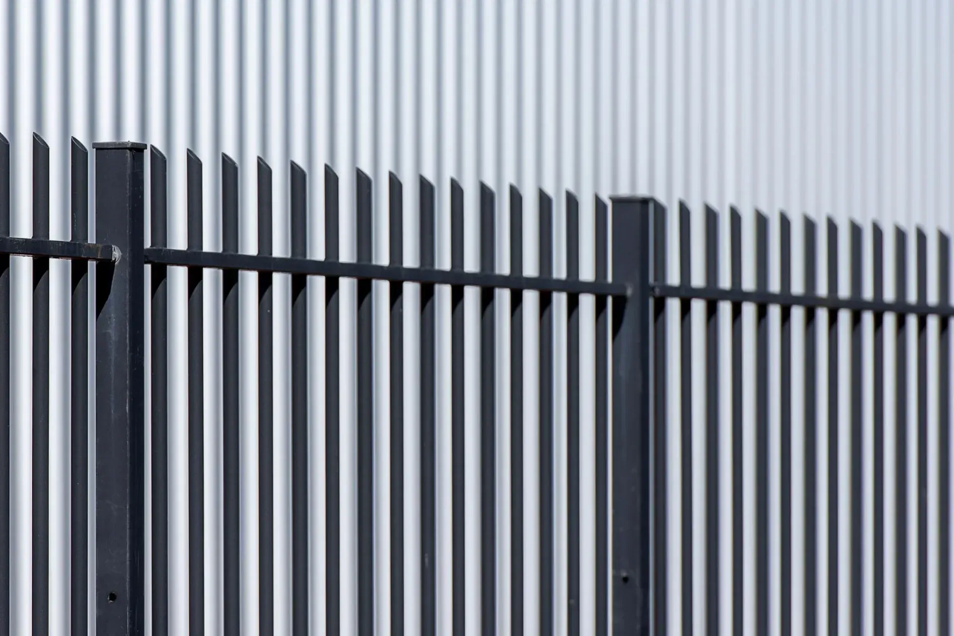Steel palisade fence in front of a clad industrial building.