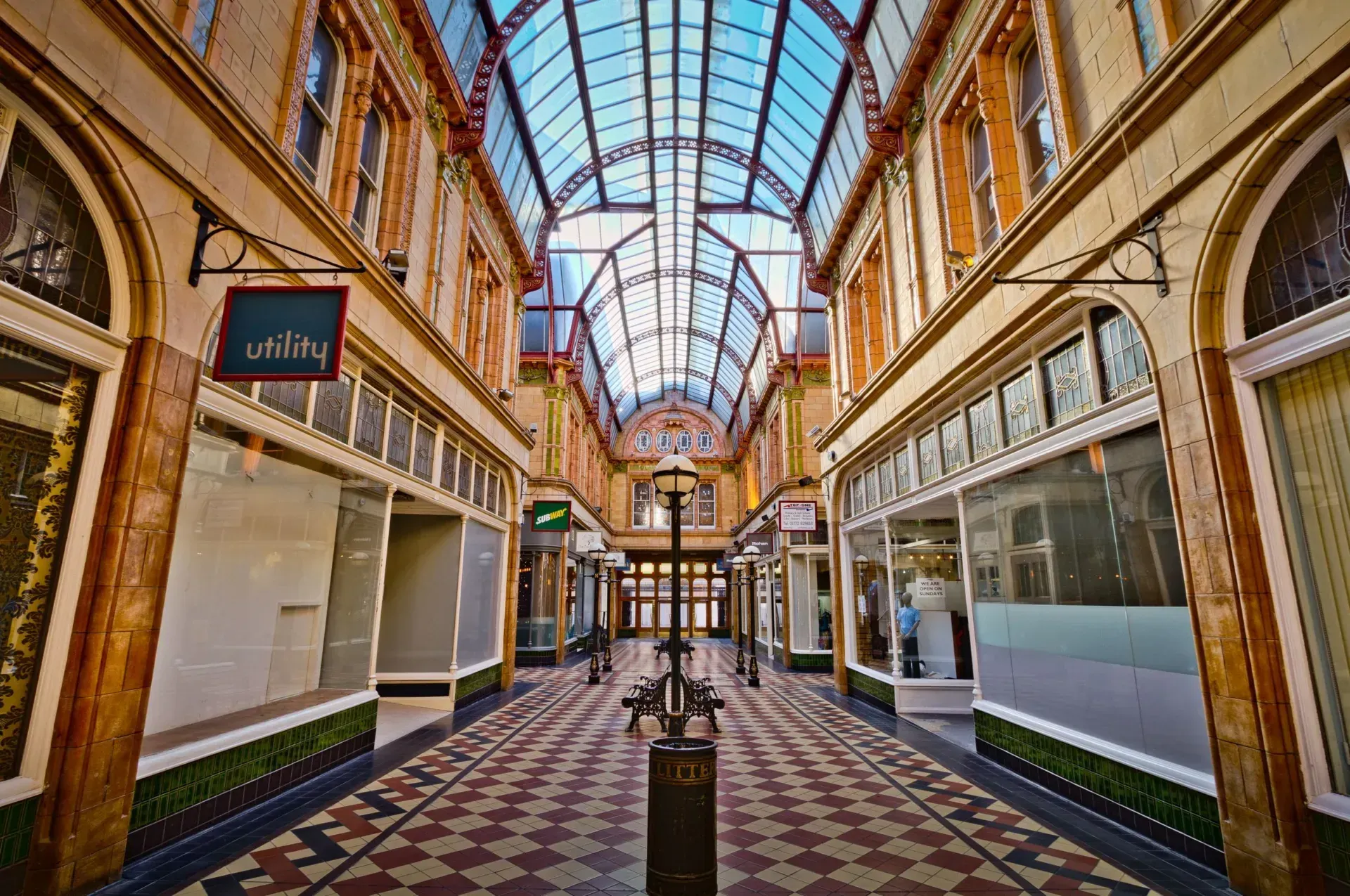 A Victorian shopping arcade with a glass roof, tiled floor and shopfronts on both sides.