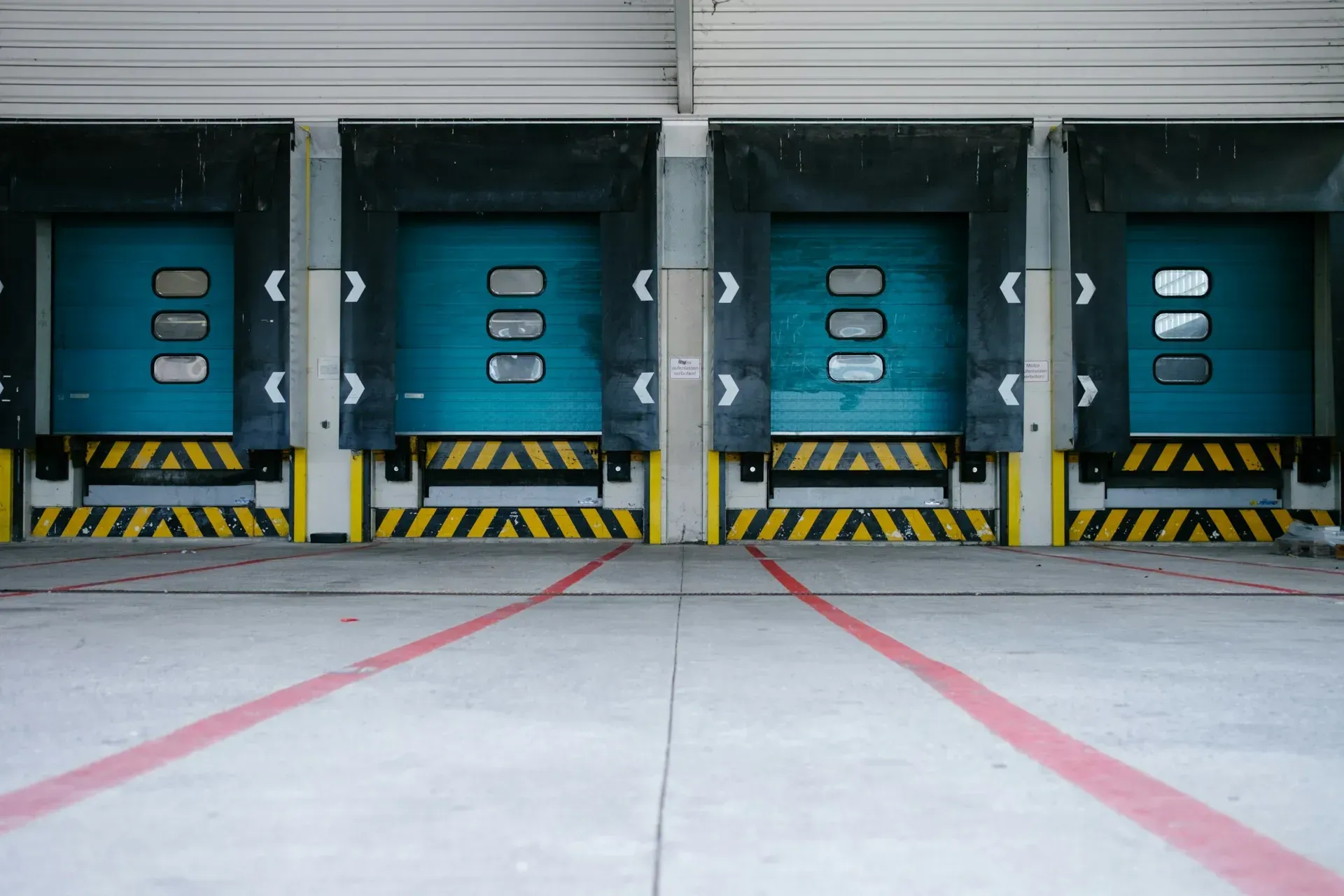 A row of closed loading bay doors with dock shelters and hazard-striped buffers.