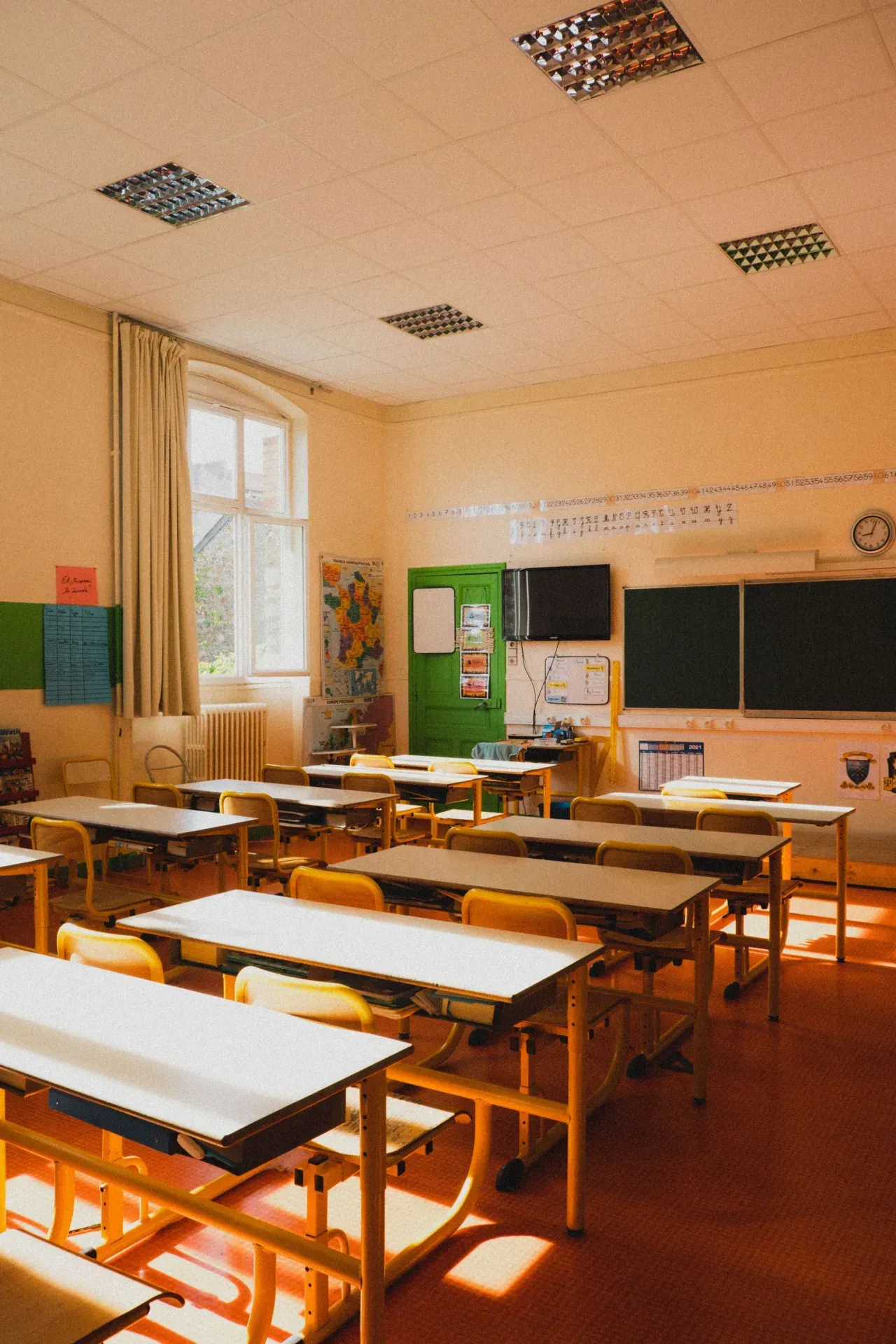 An empty, sunlit classroom with rows of desks and chairs facing the board.