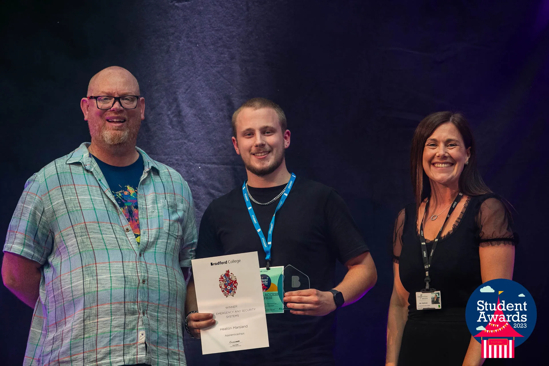 Heaton Marsland on stage with his Bradford College Apprentice of the Year award, between two of the presenters
