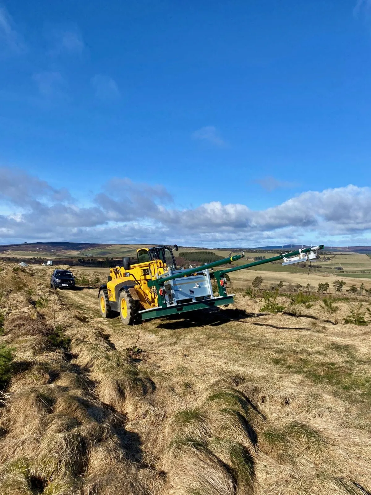 A telehandler carries the off-grid CCTV unit along a track across open moorland