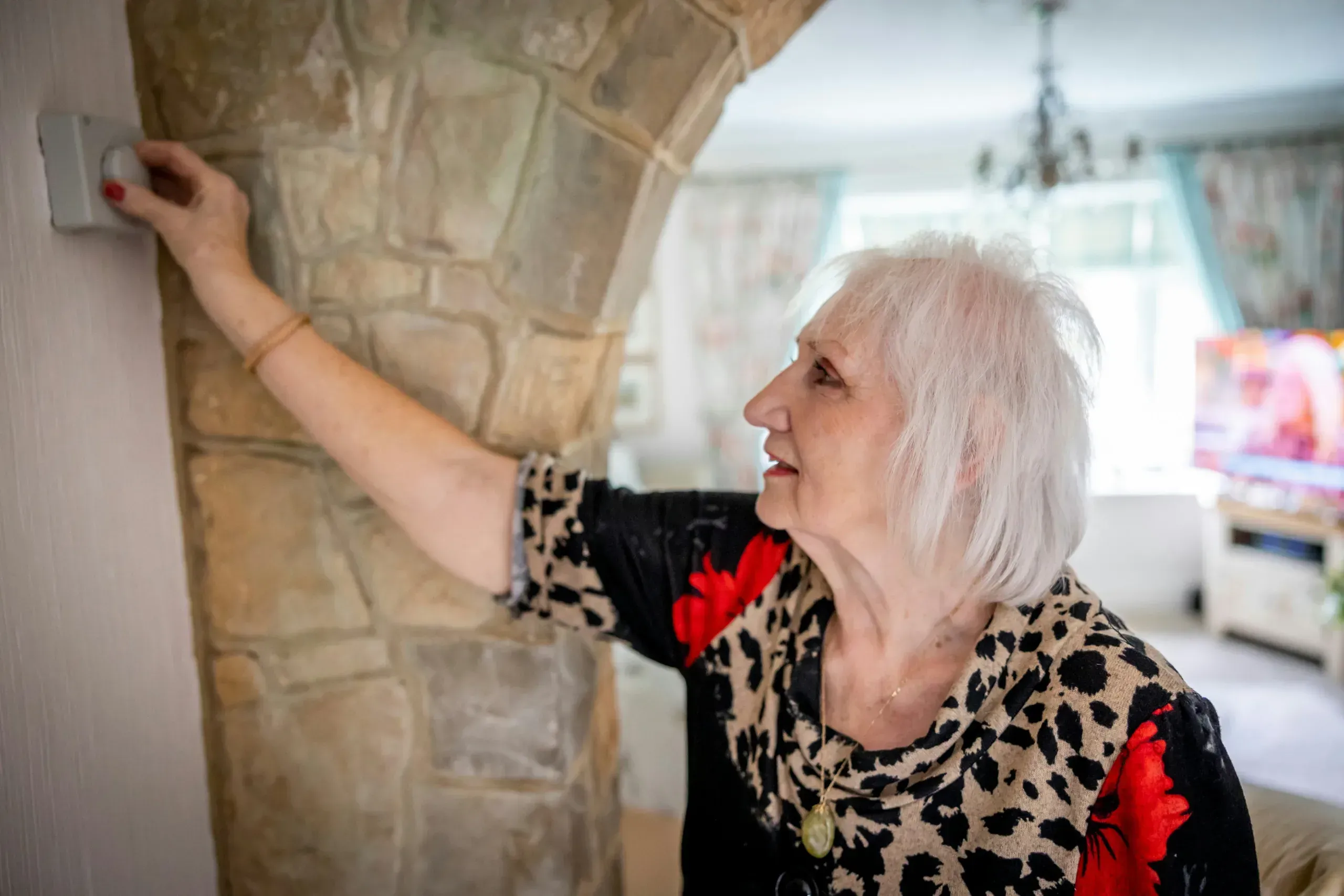 Older woman at home reaching to a wall by a window