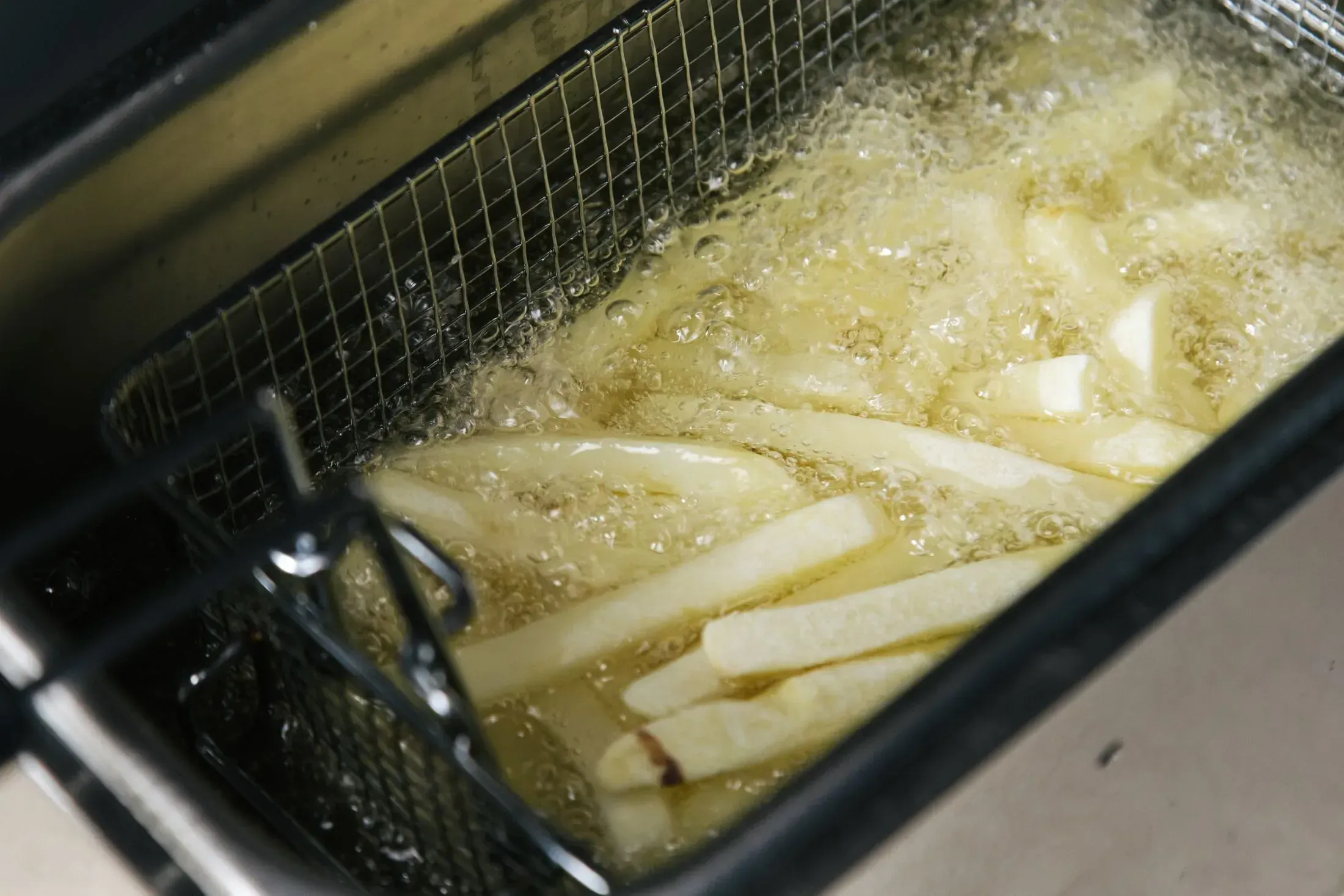 Basket of chips cooking in a stainless steel deep fryer