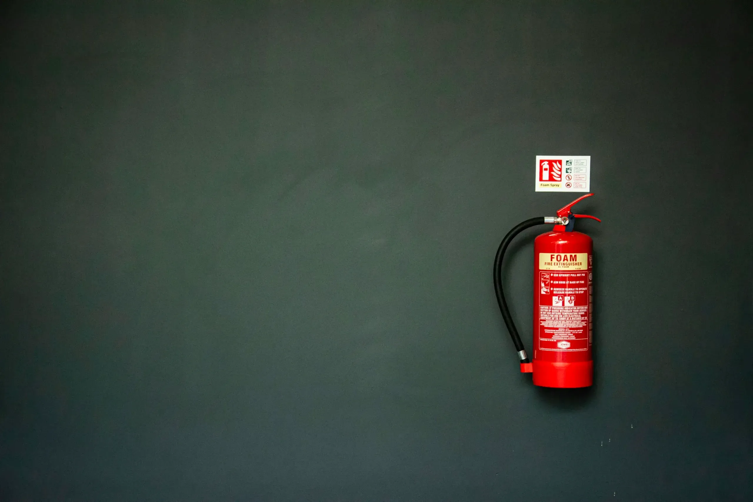 Red foam fire extinguisher with its sign on a dark wall