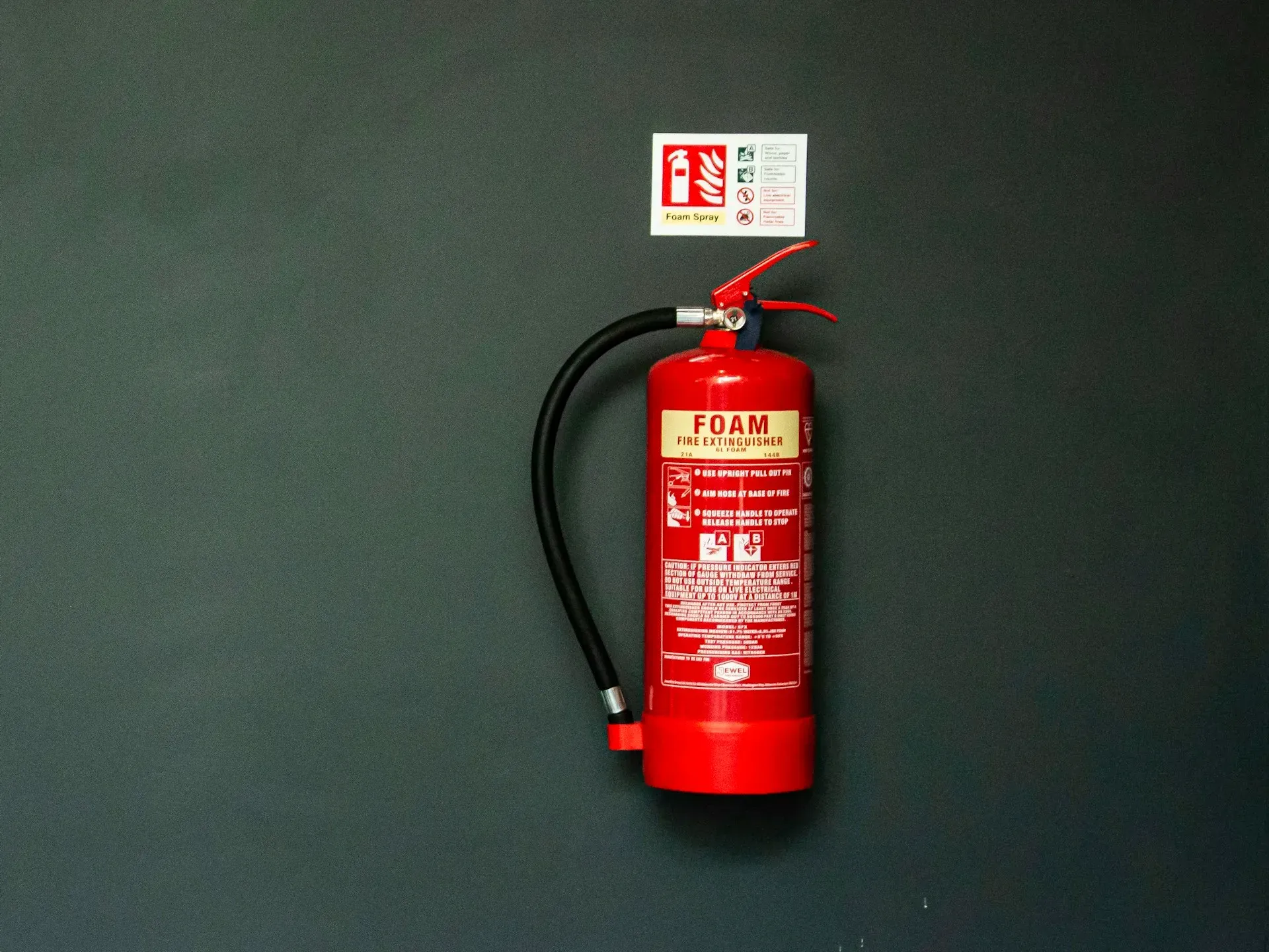 Wall-mounted foam extinguisher with its hose, handle and identification sign