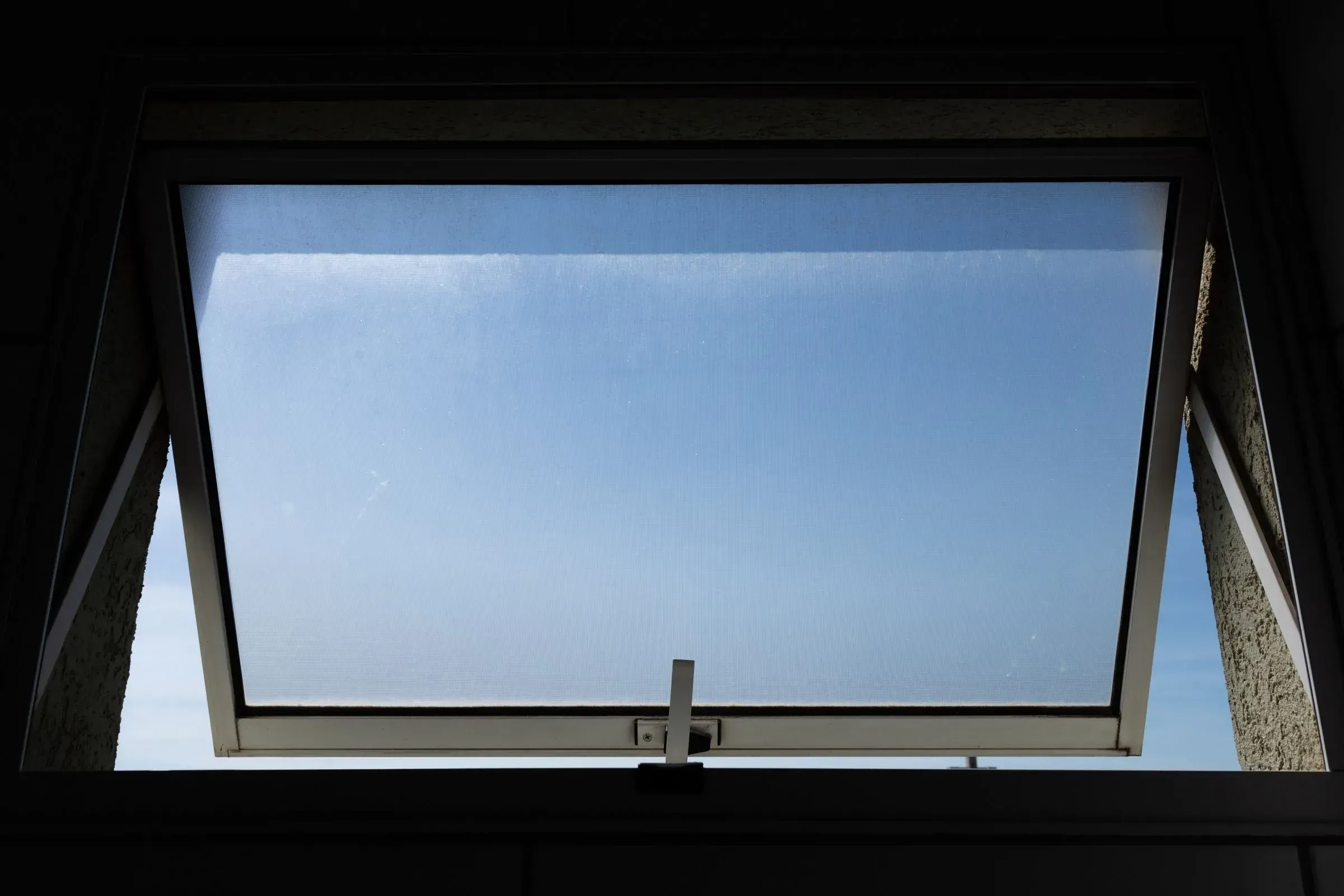 Top-hung vent window open against blue sky, seen from below