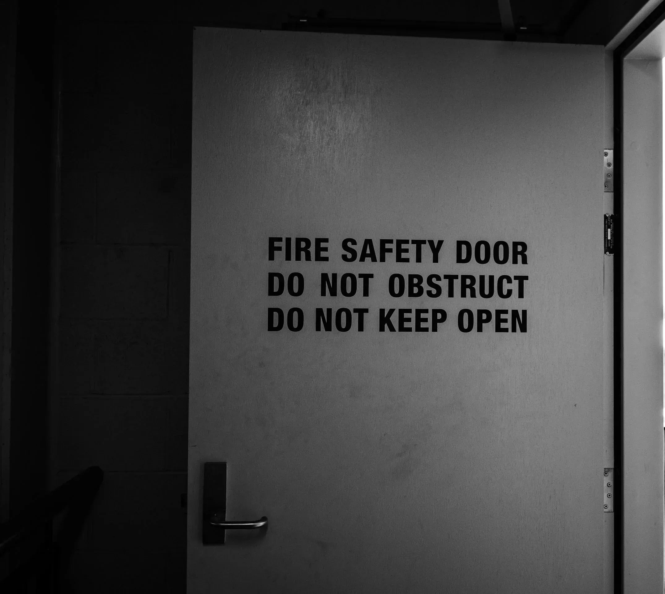 A fire door in a stairwell, signed "Fire safety door, do not obstruct, do not keep open", in black and white