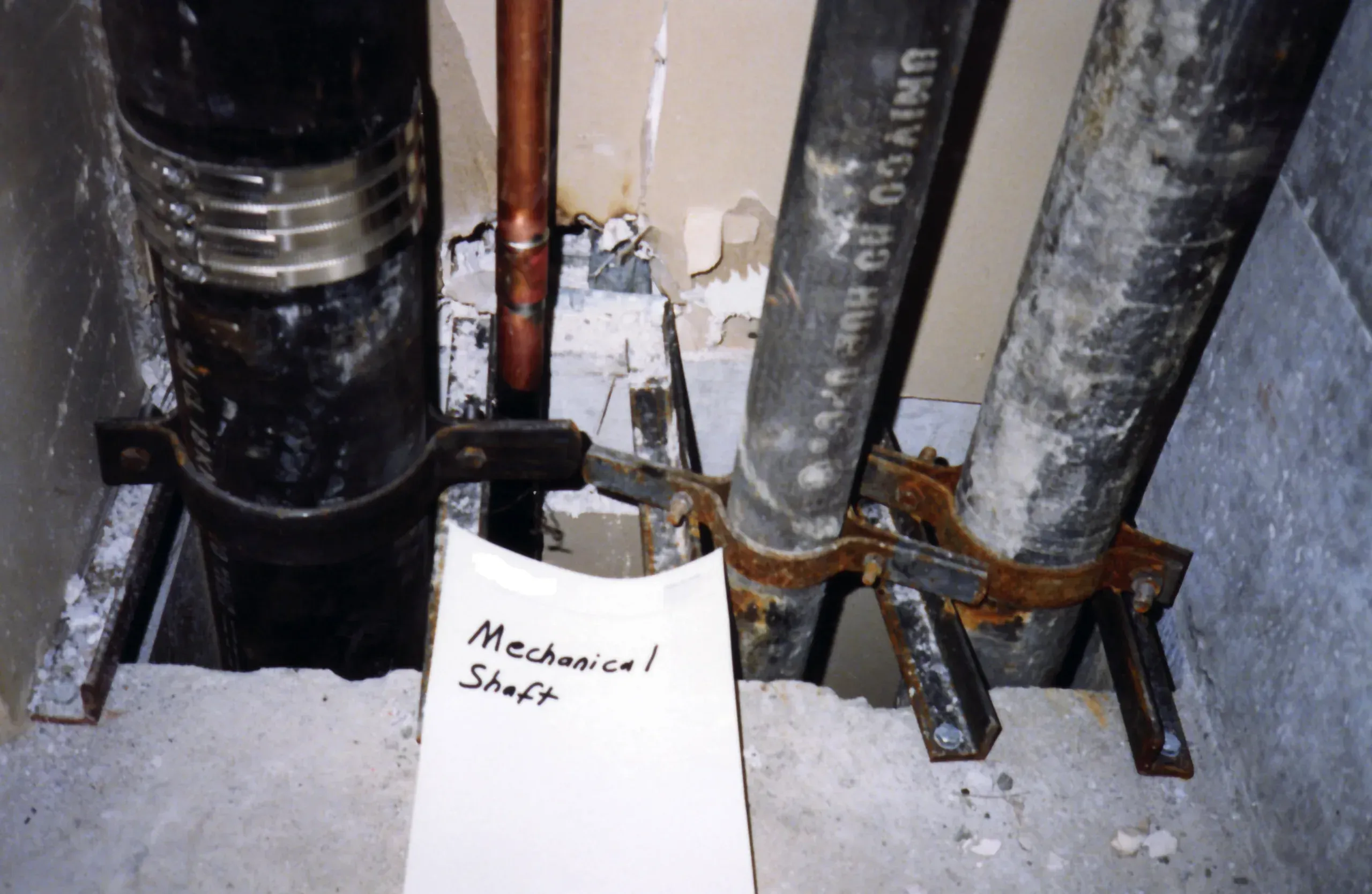 Damaged plasterboard lining around pipes in a mechanical service shaft