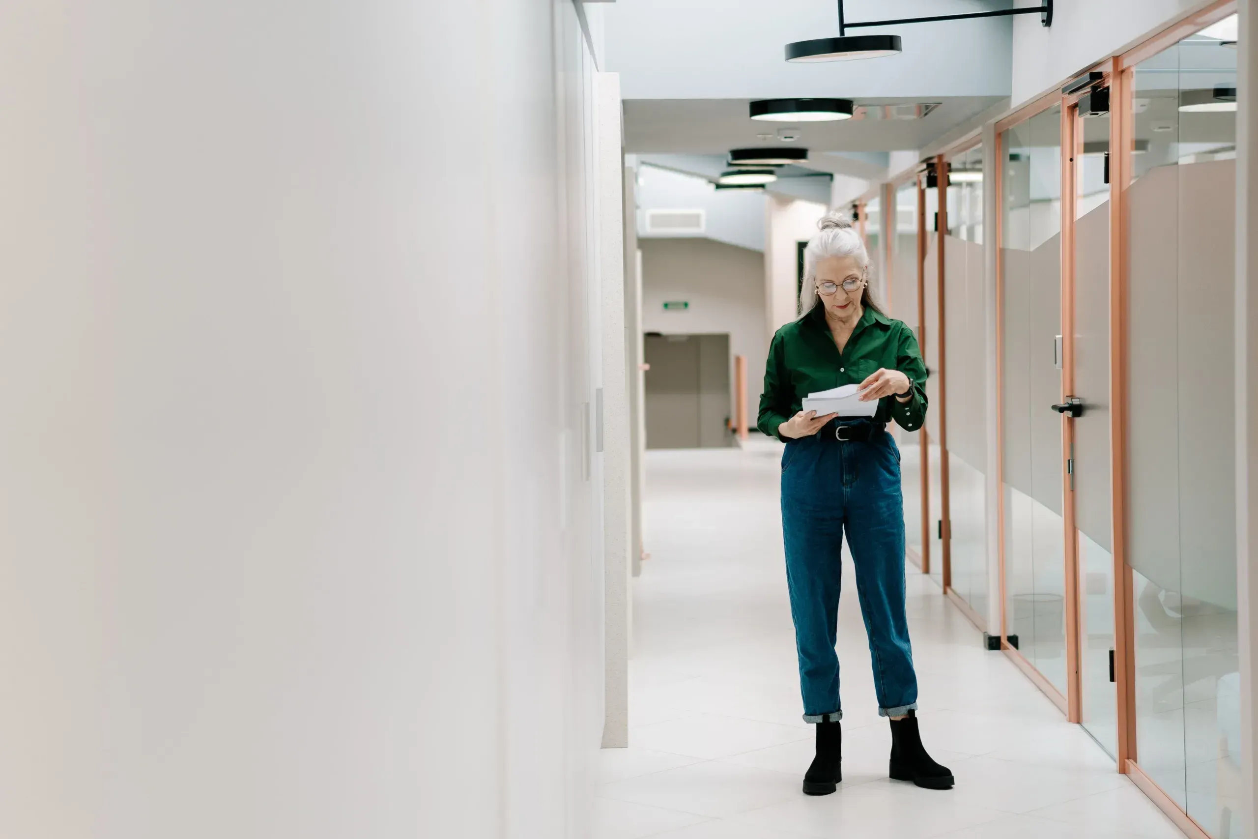 Woman reviewing papers in a bright office corridor with glazed partitions
