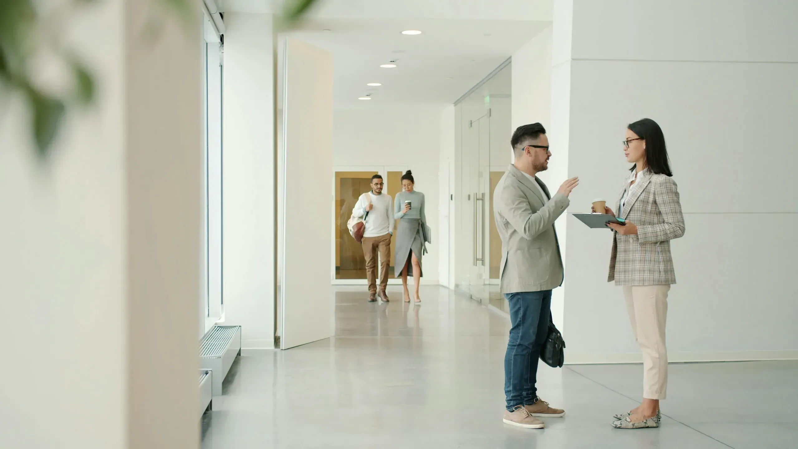 Two colleagues with a clipboard talking in a bright, modern office corridor
