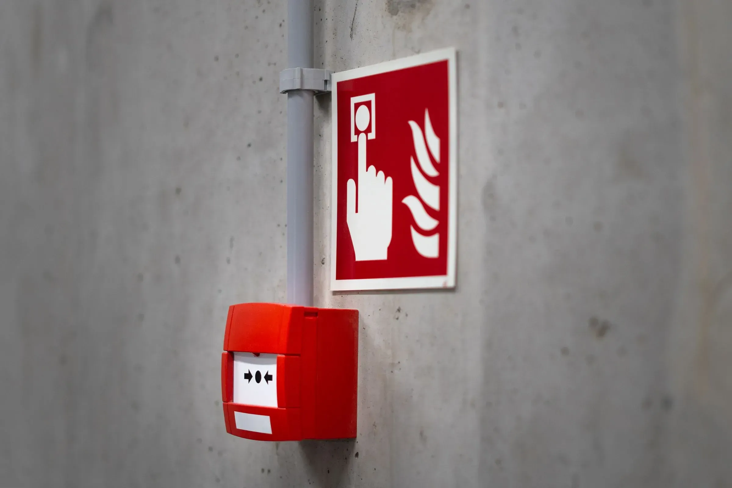 Red manual fire alarm call point and identification sign on a concrete wall