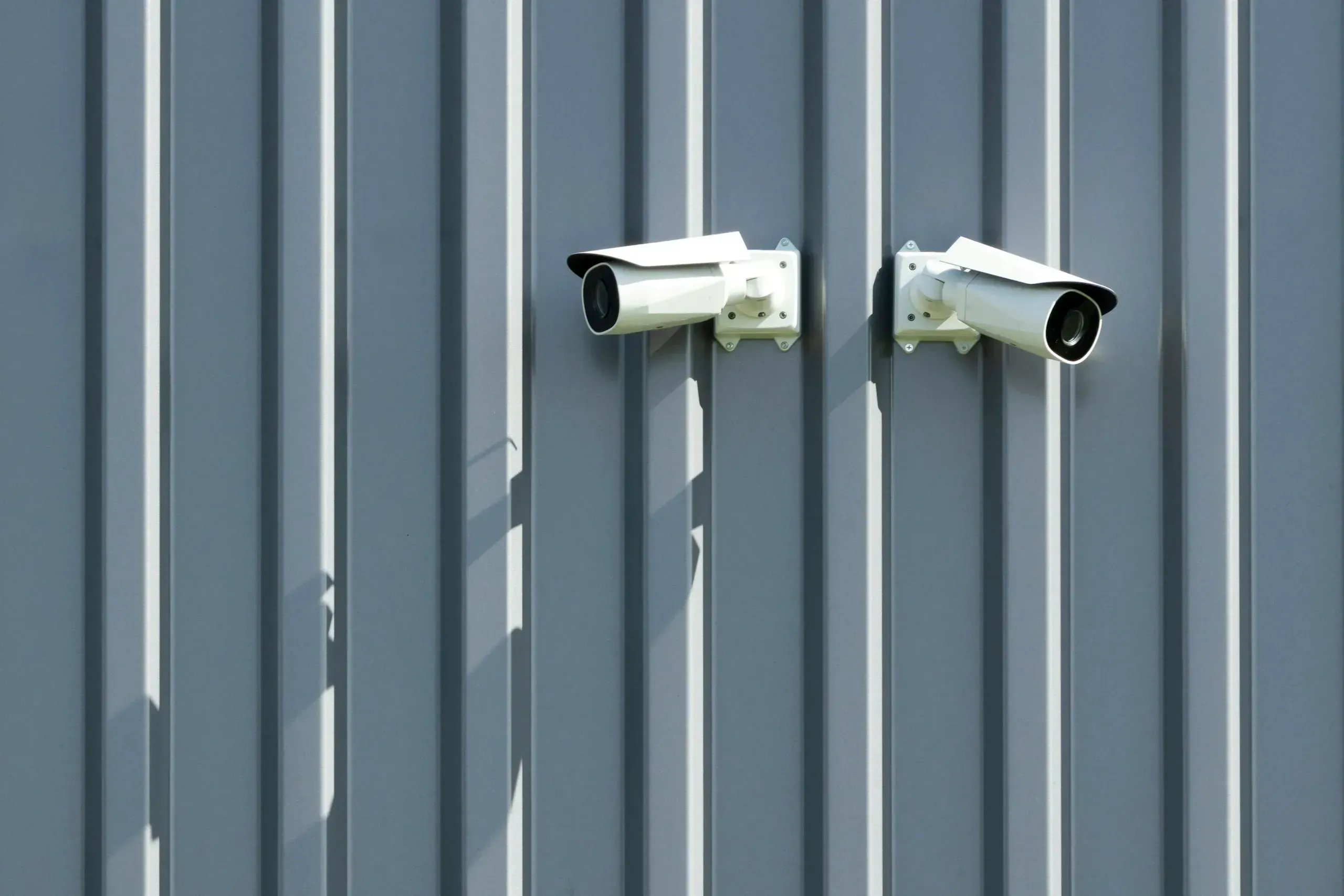 Two white bullet cameras on blue-grey steel cladding