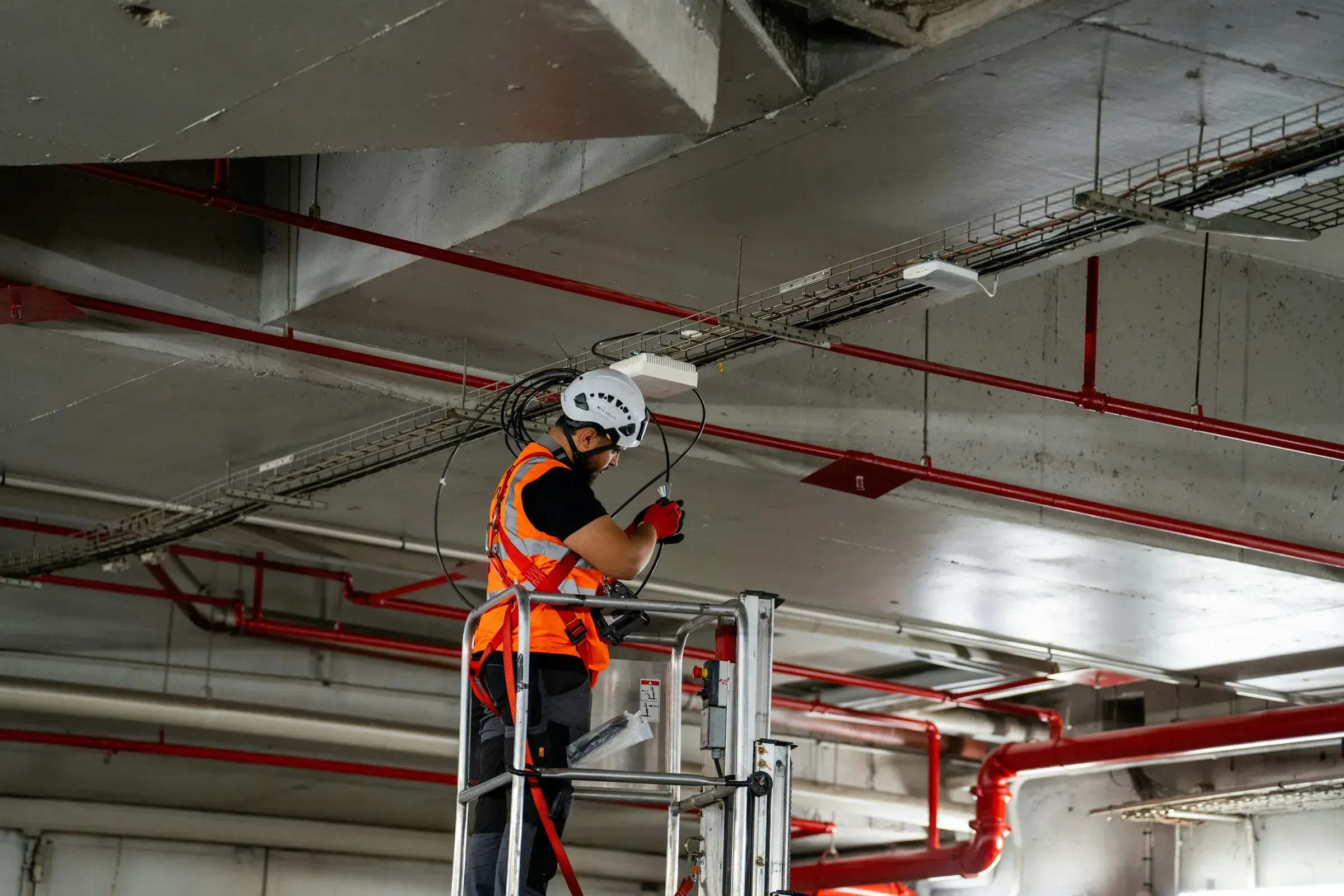 An engineer in hi-vis running cable to a ceiling device from a lift