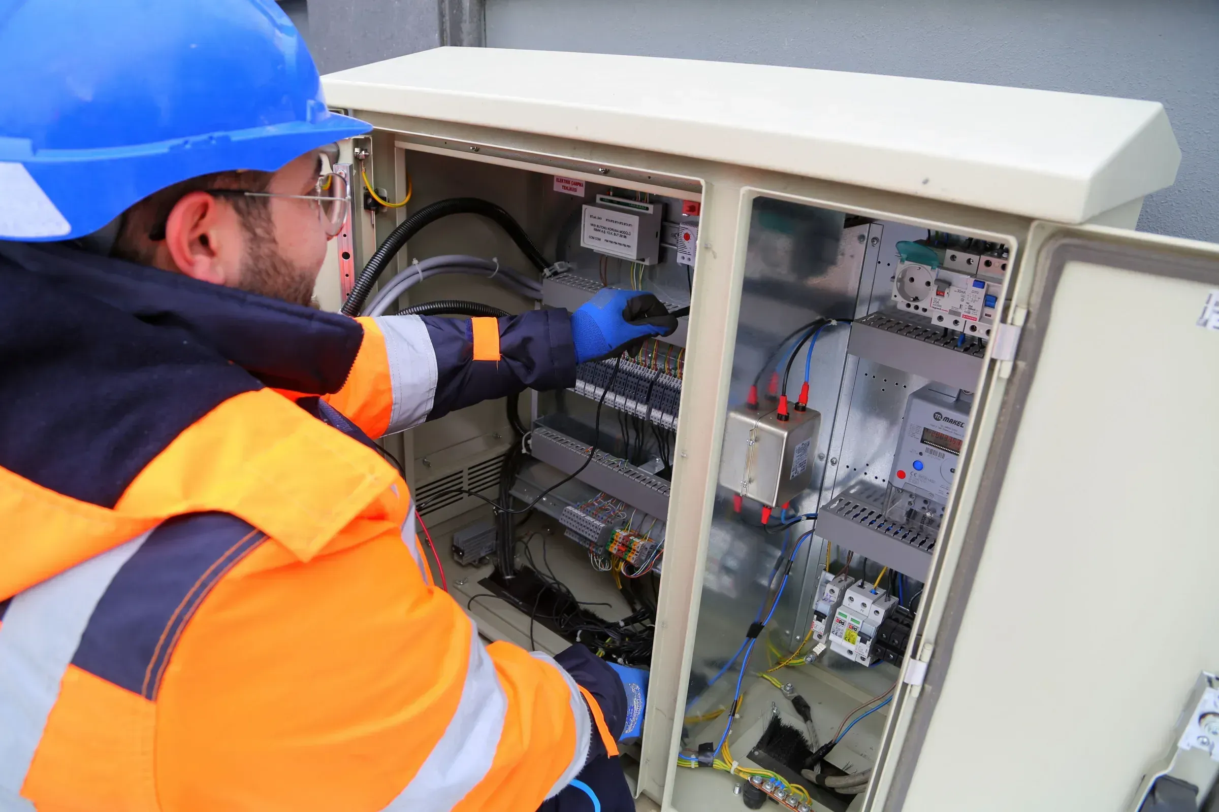 An engineer testing wiring in an open control cabinet