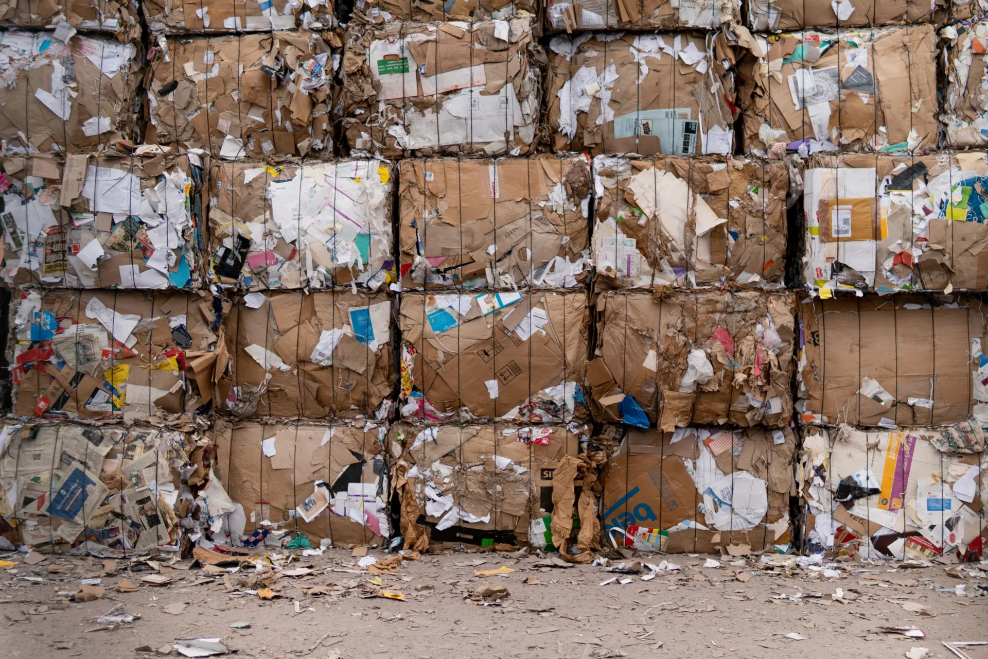 Bales of compressed cardboard and paper stacked four high at a recycling yard.