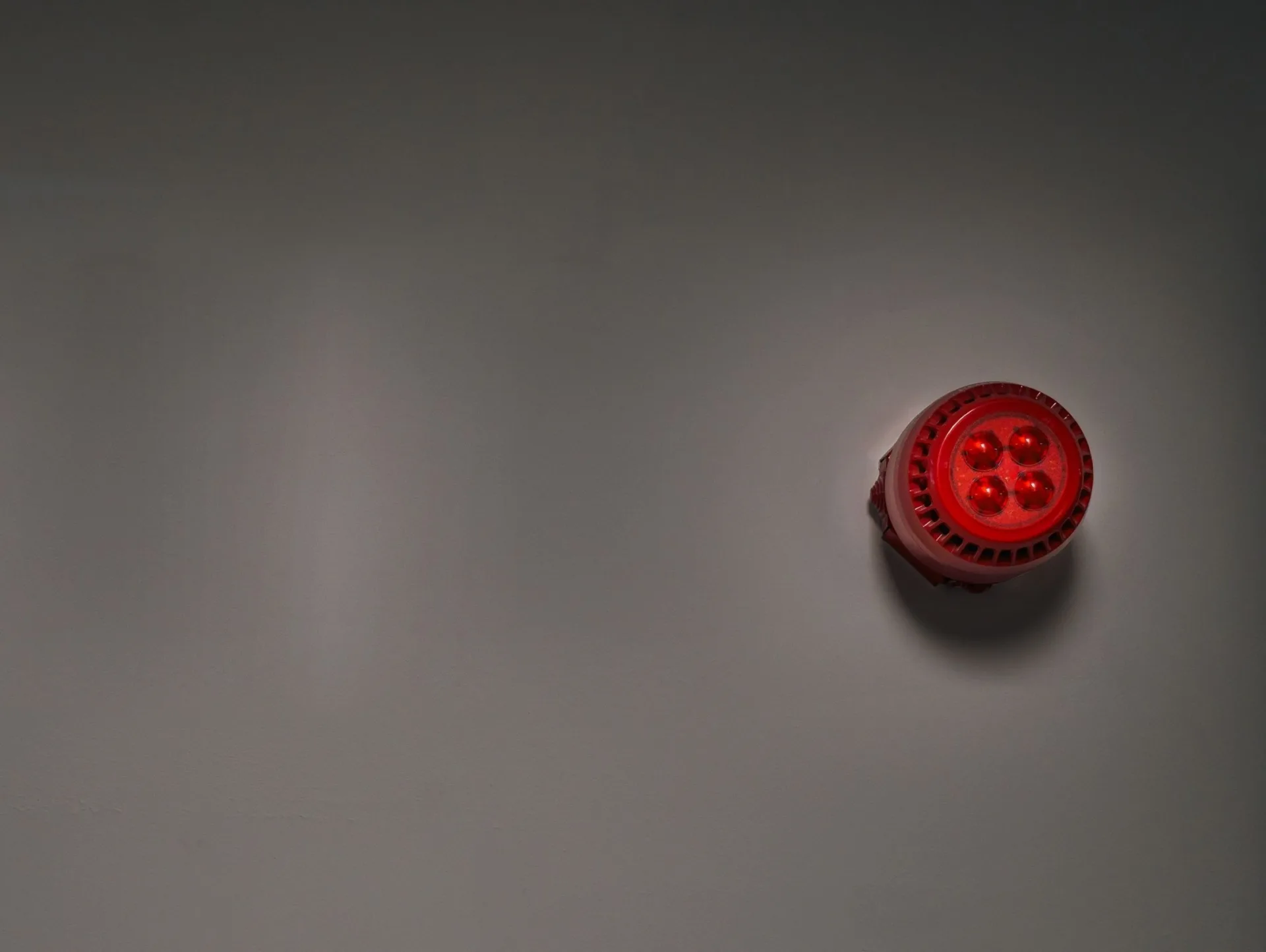 A red fire alarm sounder beacon mounted on a dark grey interior wall