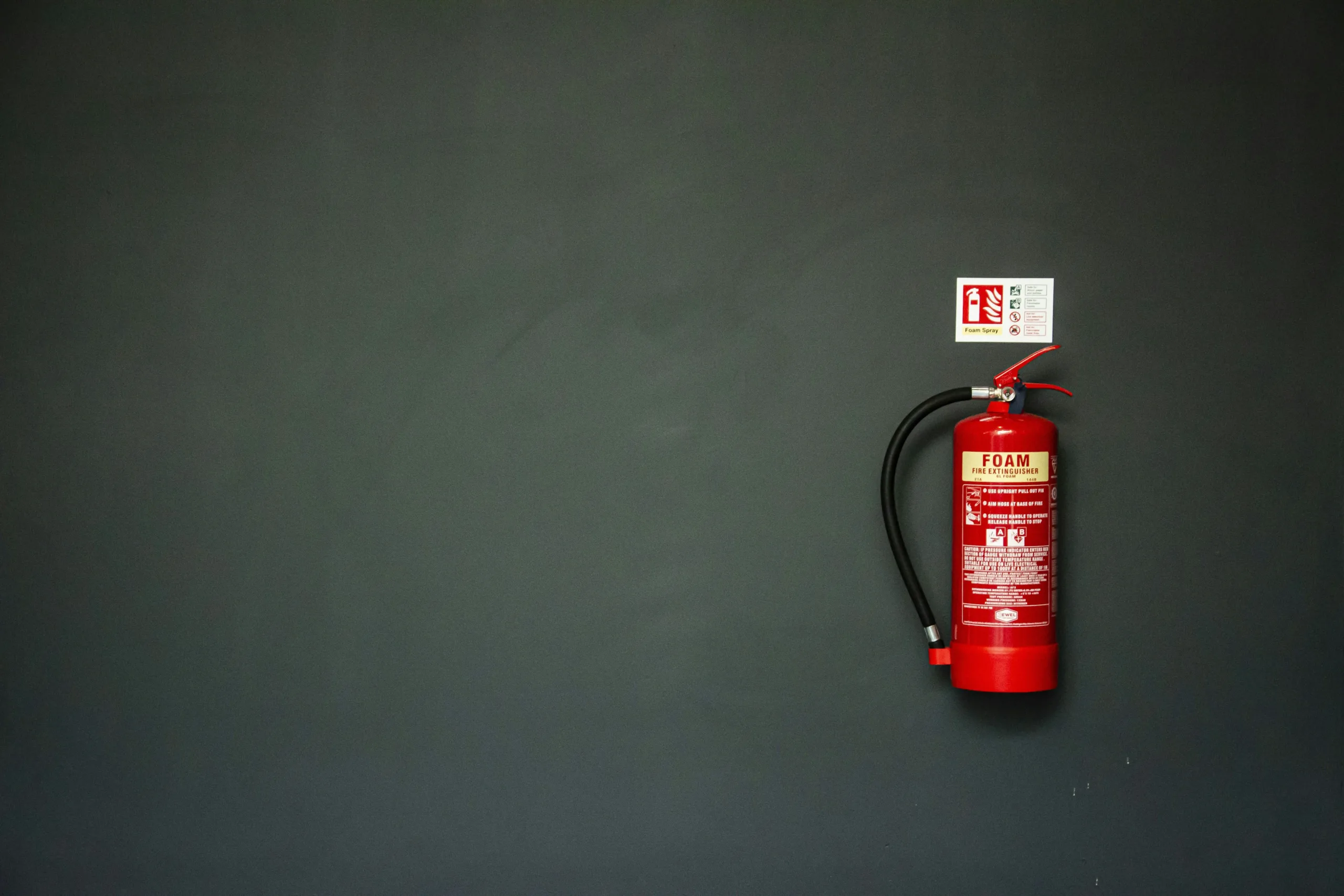 Red foam fire extinguisher with its sign on a dark wall (full-size original of today's photo)