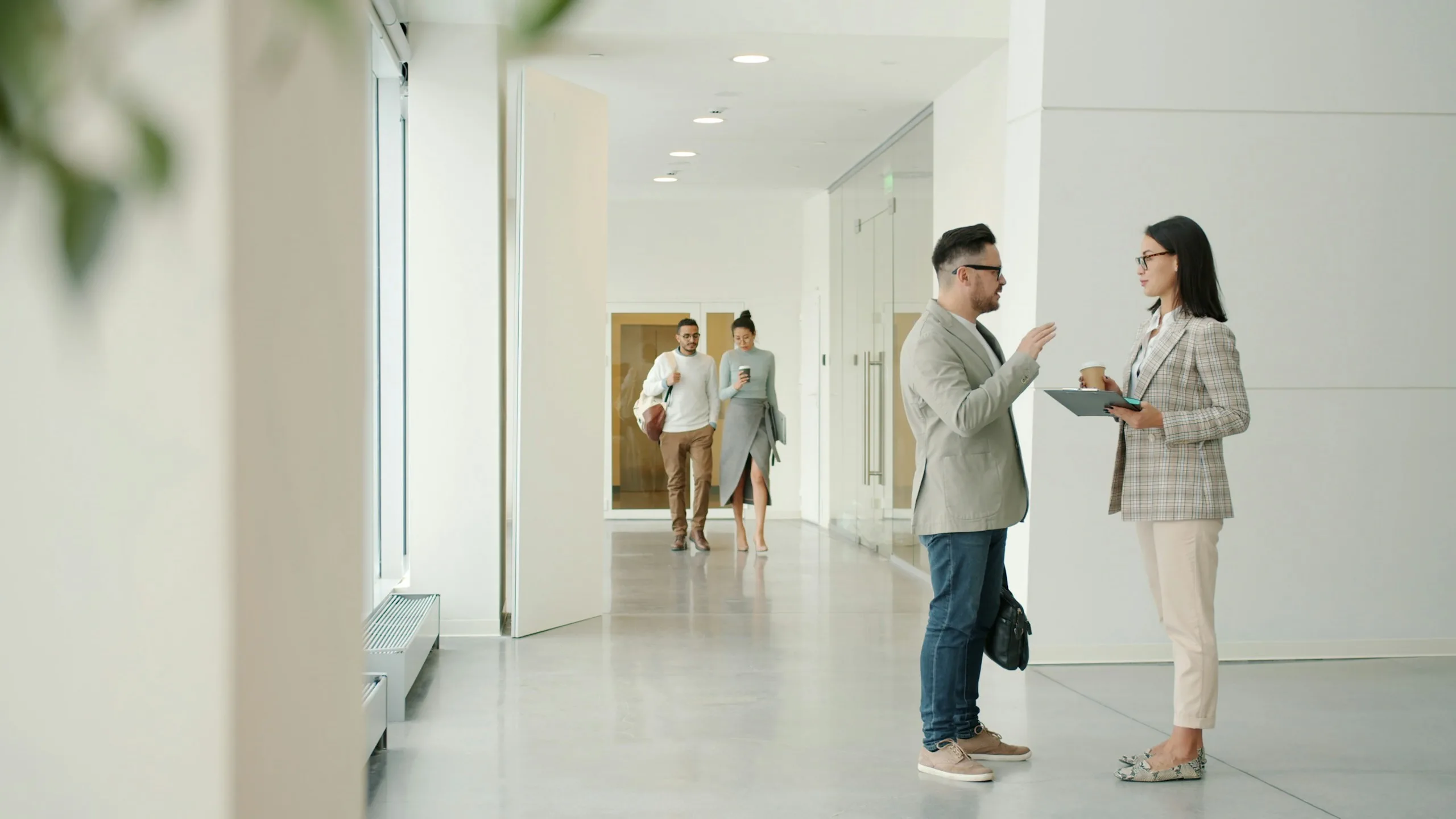Two colleagues with a clipboard talking in a bright, modern office corridor