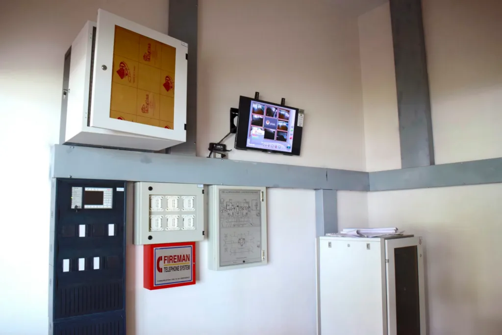 A fire alarm panel, a fireman's telephone point and a CCTV monitor mounted on a plant room wall