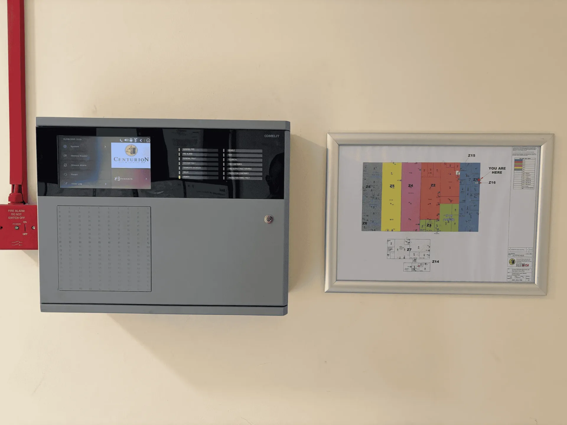 A fire alarm panel showing the Centurion logo, beside the framed zone plan of the building